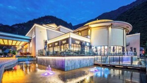 A modern hotel with a pool area, glass railings, and a mountainous backdrop. - Qianhe Rezen Hotel (Jiuzhaigou)
