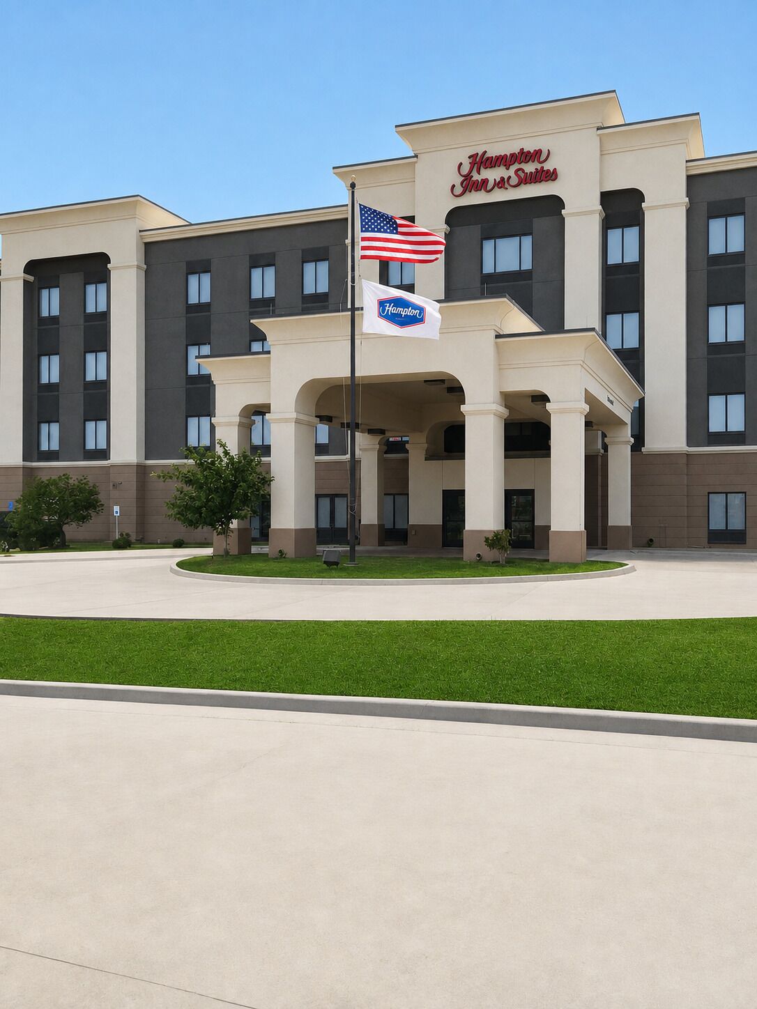 Ein Hampton Inn & Suites Hotel mit zentralem Eingang, amerikanischer Flagge und einer Flagge mit dem Hampton-Logo.