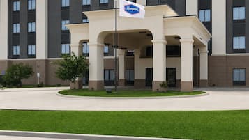 Un hôtel Hampton Inn & Suites doté d’une entrée principale, d’un drapeau américain et d’un drapeau arborant le logo Hampton.
