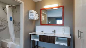 Un bagno con doccia, lavandino, specchio e asciugamani su uno scaffale.
