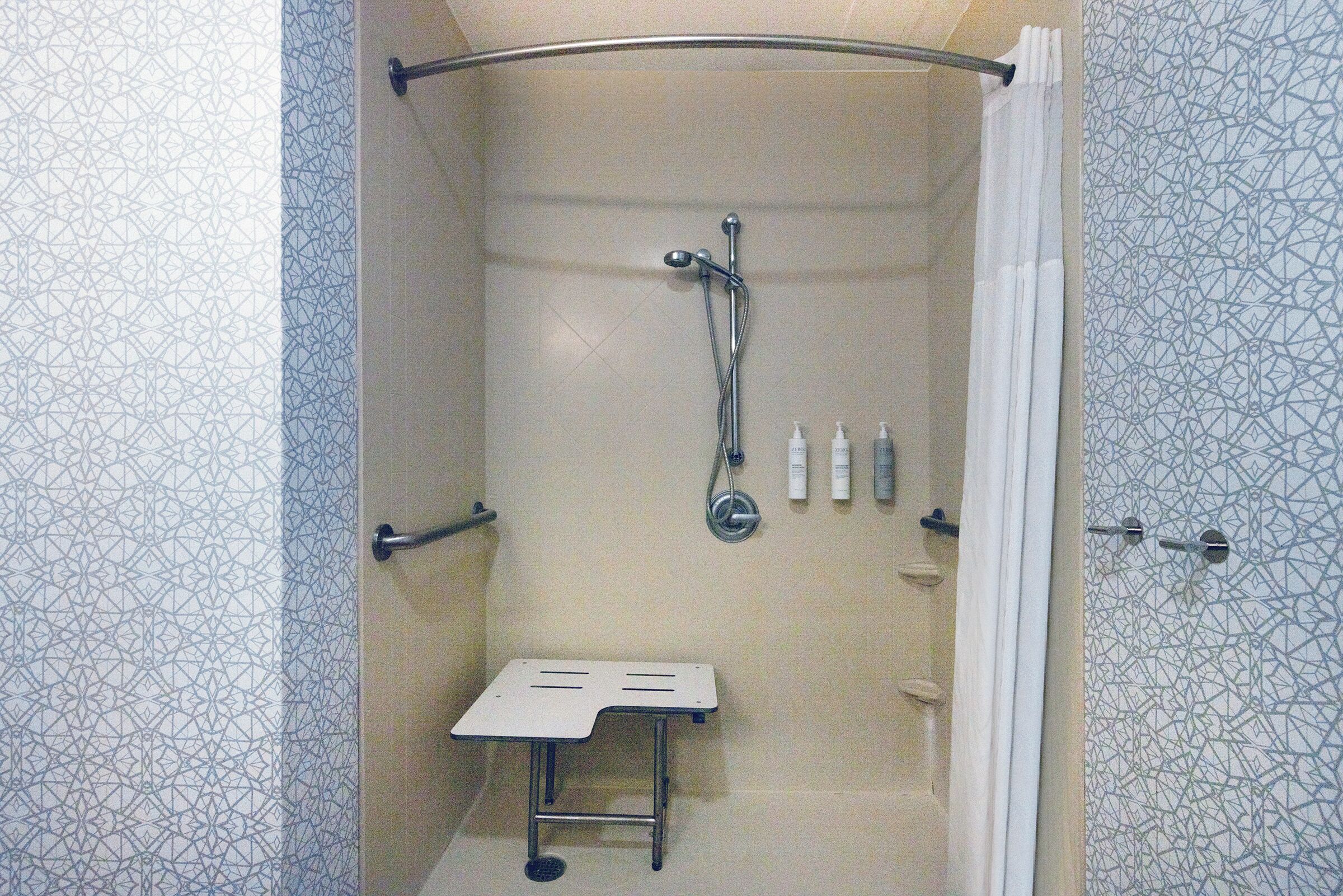 A shower with a handheld showerhead, a small table, and toiletries on the wall.