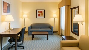 Une chambre d’hôtel avec un canapé à carreaux, une petite table, un bureau avec une lampe, une chaise et un grand miroir.