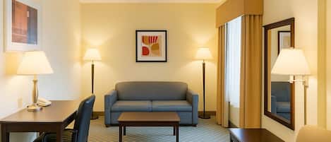 A hotel room with a checkered sofa, a small table, a desk with a lamp, a chair, and a large mirror.