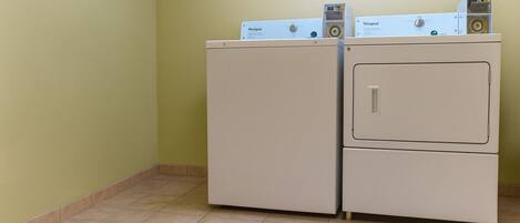 A laundry room with two stacked washers and dryers, a tiled floor, and a plain wall.