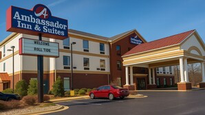 Un hôtel avec une enseigne indiquant « Ambassador Inn & Suites » et un panneau d’accueil avec l’inscription « Roll Tide ».