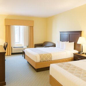 Ein Hotelzimmer mit einem großen Bett, einem kleineren Bett, einem Schreibtisch und einem Stuhl.