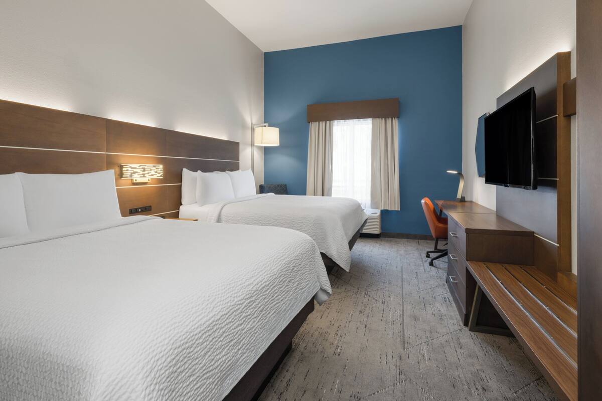 Ein Hotelzimmer mit zwei Betten, einem Schreibtisch, einem Stuhl, einem Fernseher und einem Fenster mit Vorhängen.