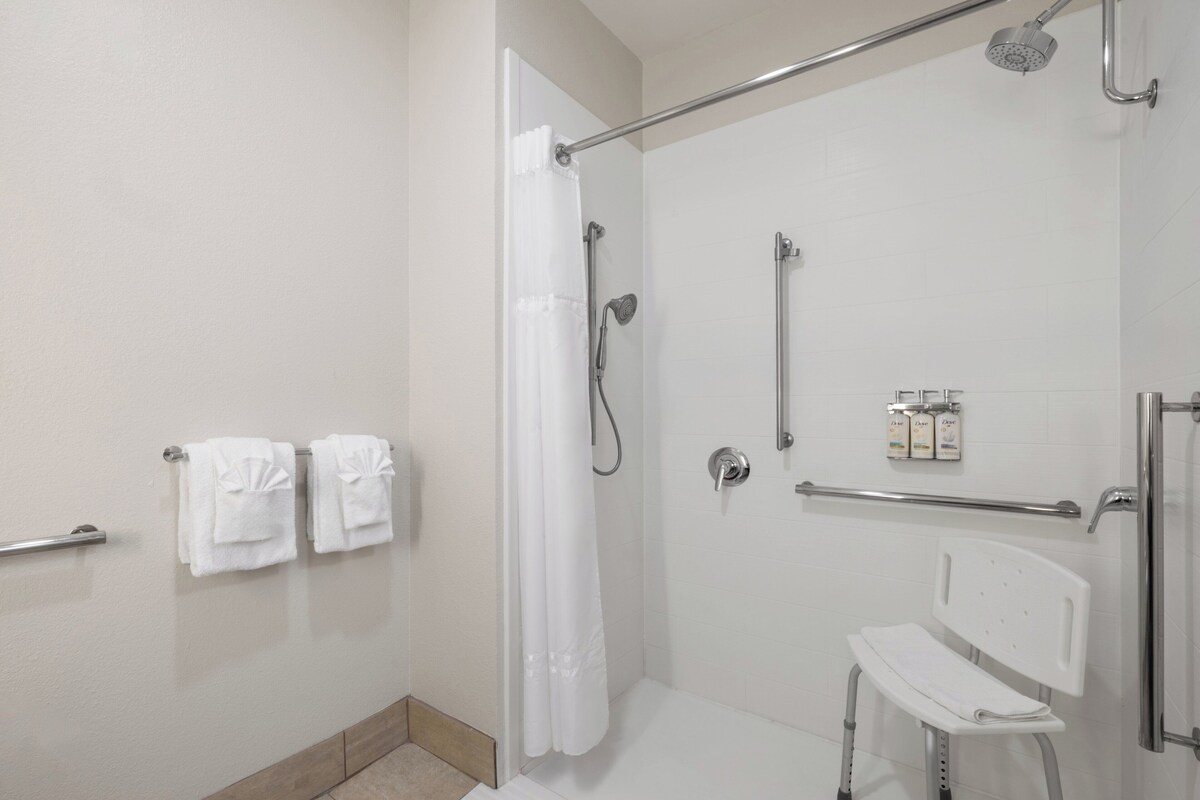 Un espace douche doté d’une porte en verre, d’une chaise blanche et de deux serviettes posées sur un porte-serviettes.