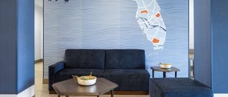 A modern room with a dark blue sofa, a wooden coffee table, and a matching ottoman. A map mural adorns the wall.
