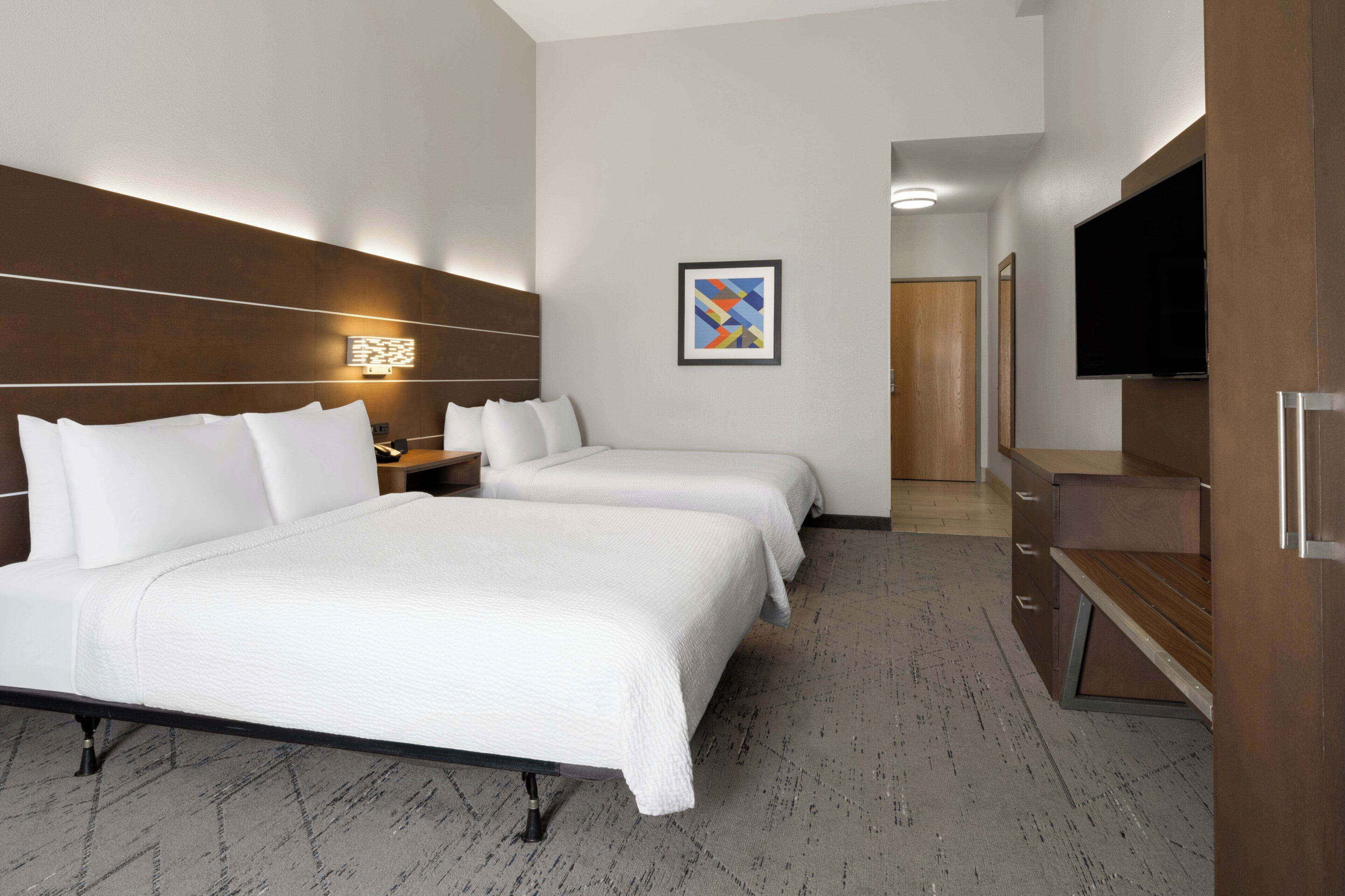 A hotel room with two beds, a TV, a wooden headboard, a framed picture, and a mirror.