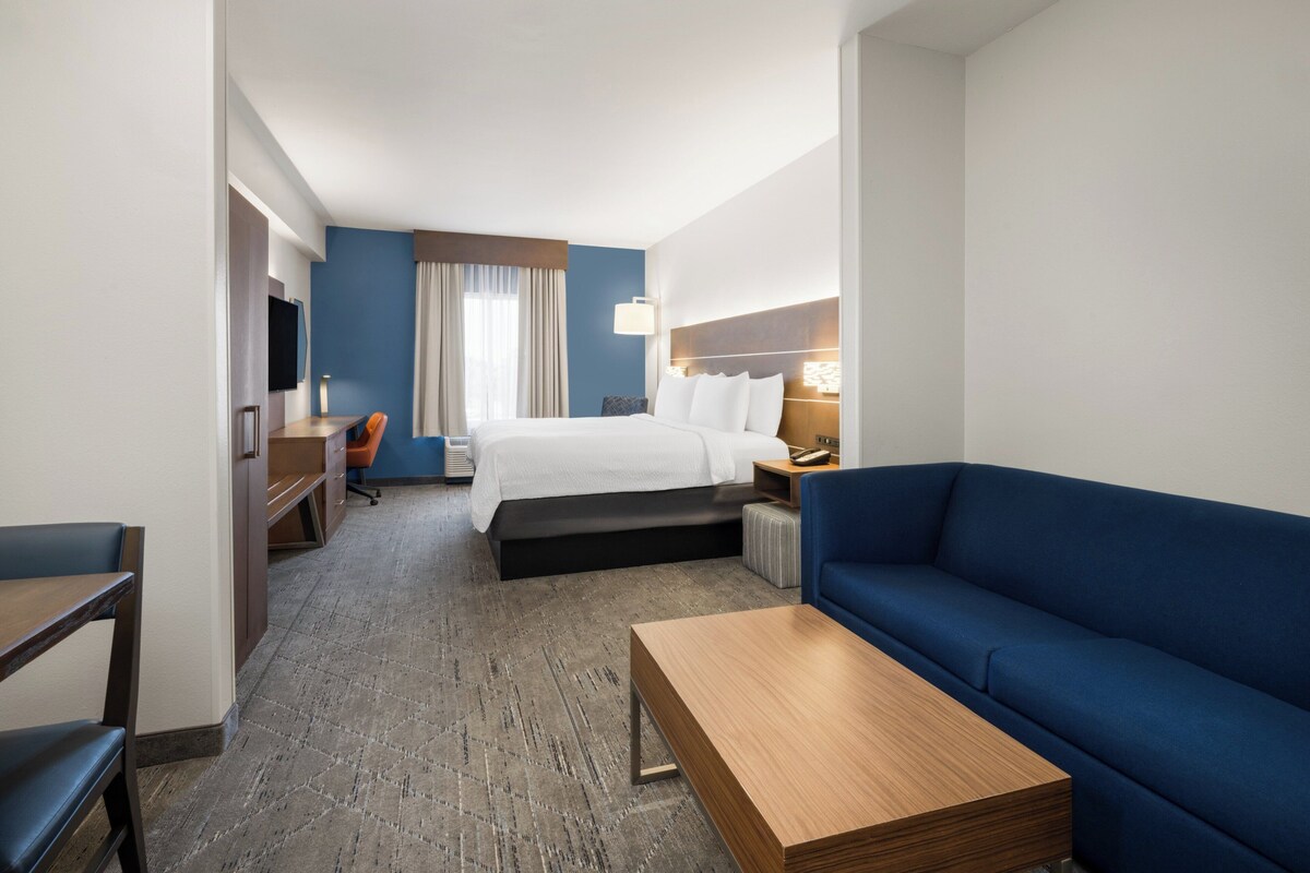 Une chambre d’hôtel avec un lit, un canapé bleu, une table basse en bois, un bureau avec une chaise et un téléviseur.