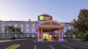 Ein Holiday Inn Express Hotel mit überdachter Einfahrt, Parkplatz und Palmen.