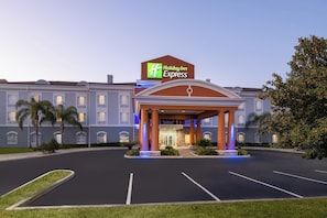 Een Holiday Inn Express hotel met een overdekte ingang, parkeerplaats en palmbomen.