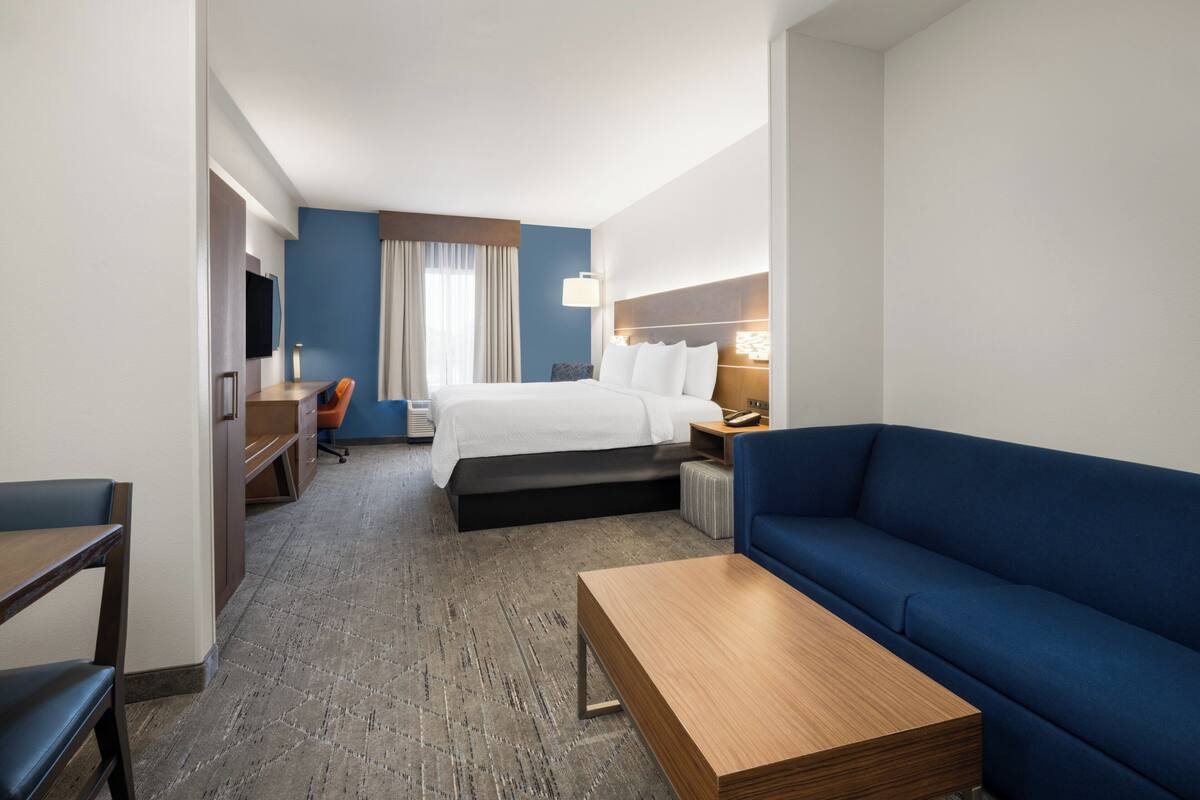 Ein Hotelzimmer mit einem Bett, einem blauen Sofa, einem Holztisch, einem Schreibtisch mit Stuhl und einem Fernseher.