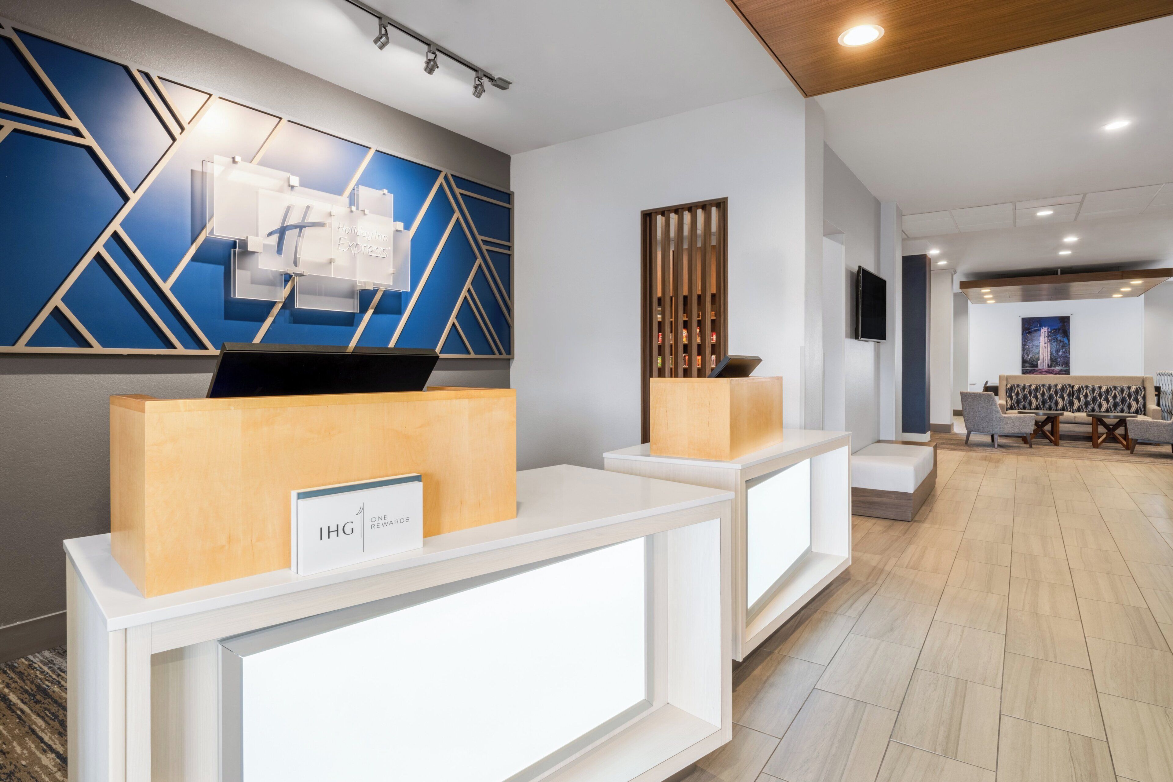 A reception area with modern design, including a blue geometric wall, wooden reception desks, and a seating area with patterned sofas.