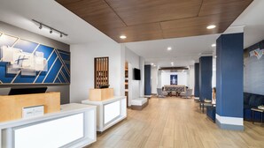 Un espace d’accueil moderne, avec un comptoir en bois, un coin salon avec une table et des chaises, et un grand mur orné de motifs géométriques.