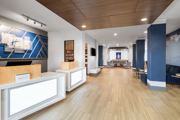 Ein moderner Hotel-Empfangsbereich mit einer Holztresen, einer Sitzecke mit Tisch und Stühlen sowie einer großen Wand mit geometrischen Mustern.