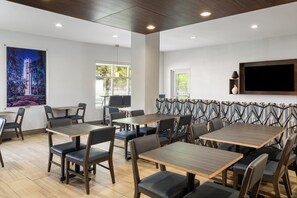 Een restaurant met tafels en stoelen, een groot schilderij en een televisie aan de muur.