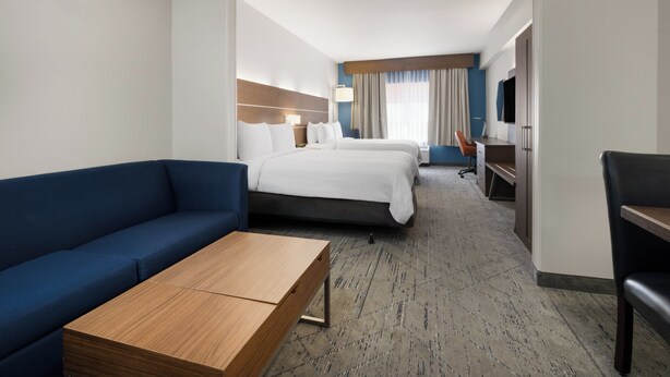 Une chambre d’hôtel avec un canapé, deux lits, un bureau, une télévision et un sol recouvert de moquette.