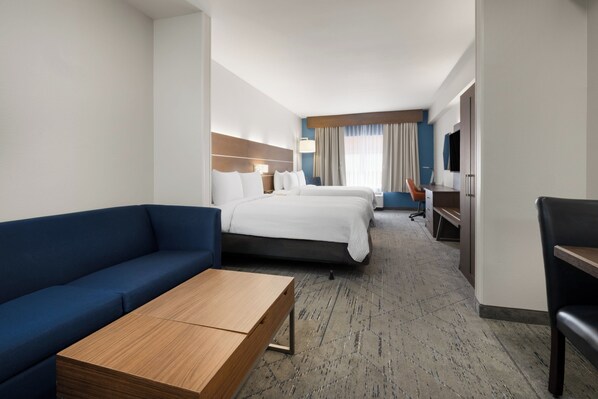 Ein Hotelzimmer mit einer Couch, zwei Betten, einem Schreibtisch, einem Fernseher und Teppichboden.