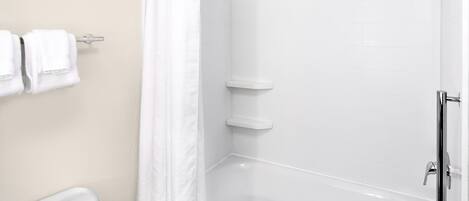 Un baño moderno con azulejos blancos, una ducha con cabezal de ducha manual y un inodoro con toallero.