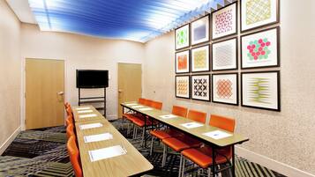 Un salón de conferencias con una larga mesa, sillas naranjas, un televisor de pantalla plana y obras de arte enmarcadas en las paredes.
