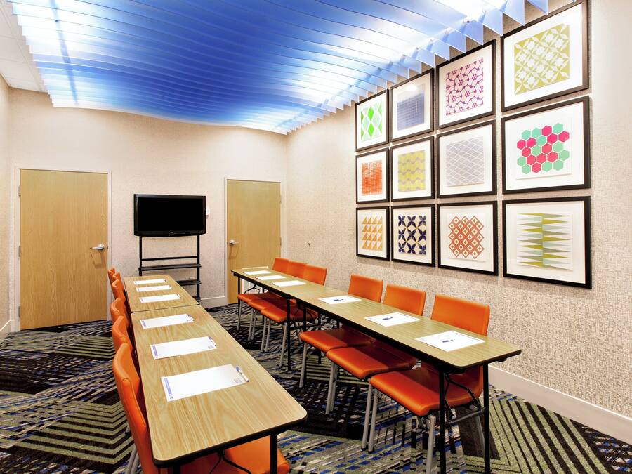 Un salón de conferencias con una larga mesa, sillas naranjas, un televisor de pantalla plana y obras de arte enmarcadas en las paredes.