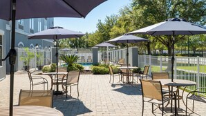 Un espace extérieur aménagé en terrasse, avec des tables et des chaises, des parasols, et une piscine en arrière-plan.