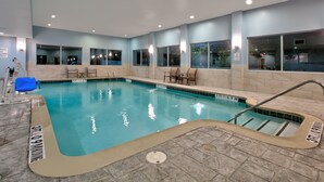 An indoor swimming pool with clear water, tiled walls, and a tiled floor. There are chairs and a blue chair near the pool. - Holiday Inn Express & Suites North Dallas at Preston by IHG (Dallas)