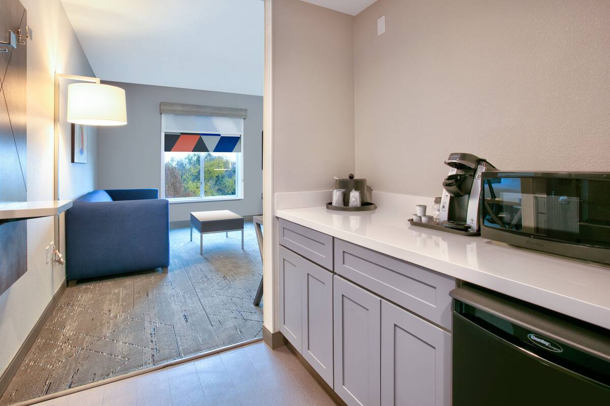 A modern kitchen with white cabinets, a built-in microwave, and a dishwasher. There is a window with a colorful view outside.