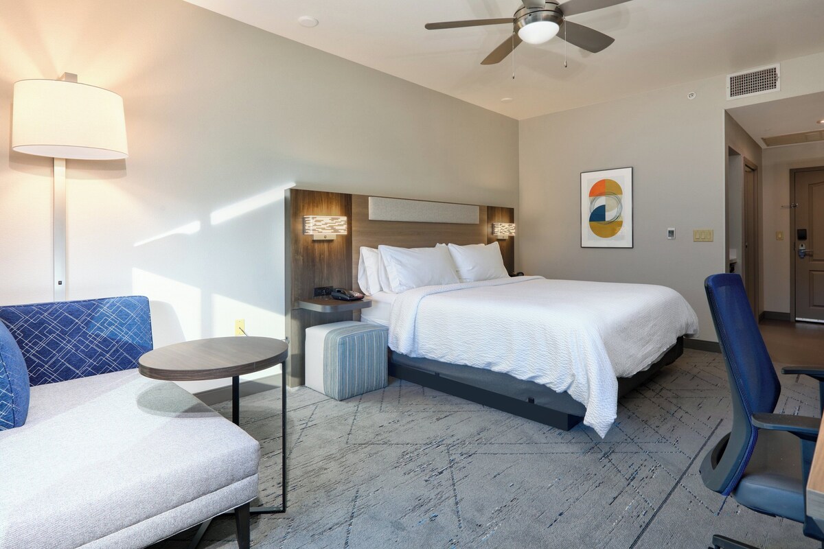 A modern hotel room with a bed, a sofa, a small table, and a ceiling fan.