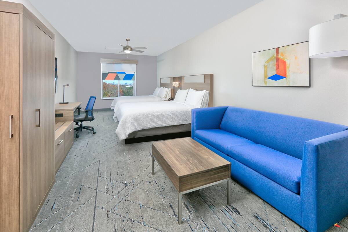 A hotel room with a bed, a blue sofa, a wooden coffee table, a desk with a chair, and a wardrobe.