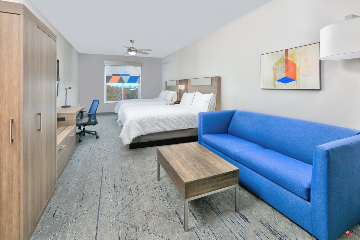 A hotel room with a bed, a blue sofa, a wooden coffee table, a desk with a chair, and a wardrobe.