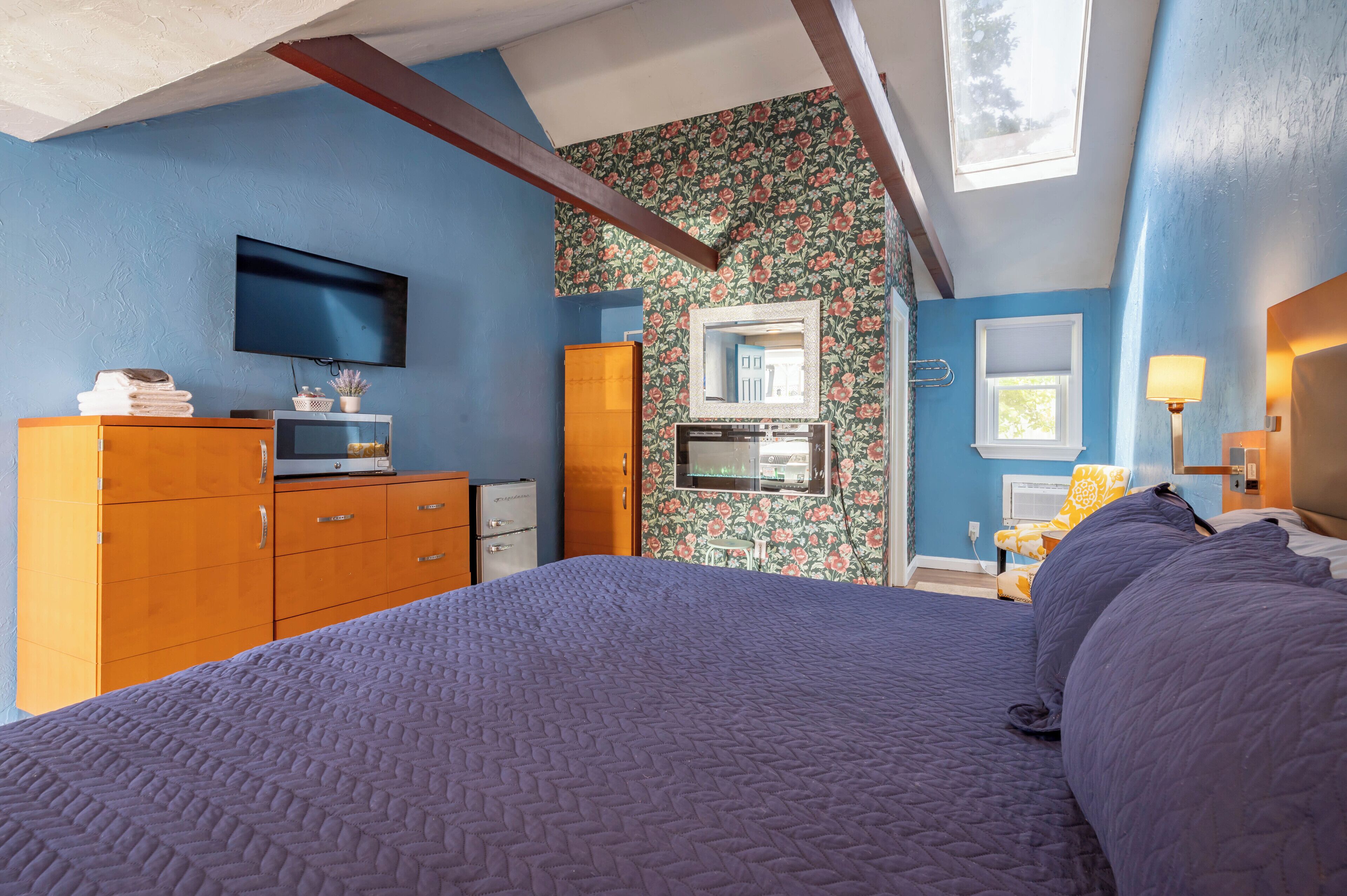 Un dormitorio con cama, televisión, cómoda, espejo y ventana.