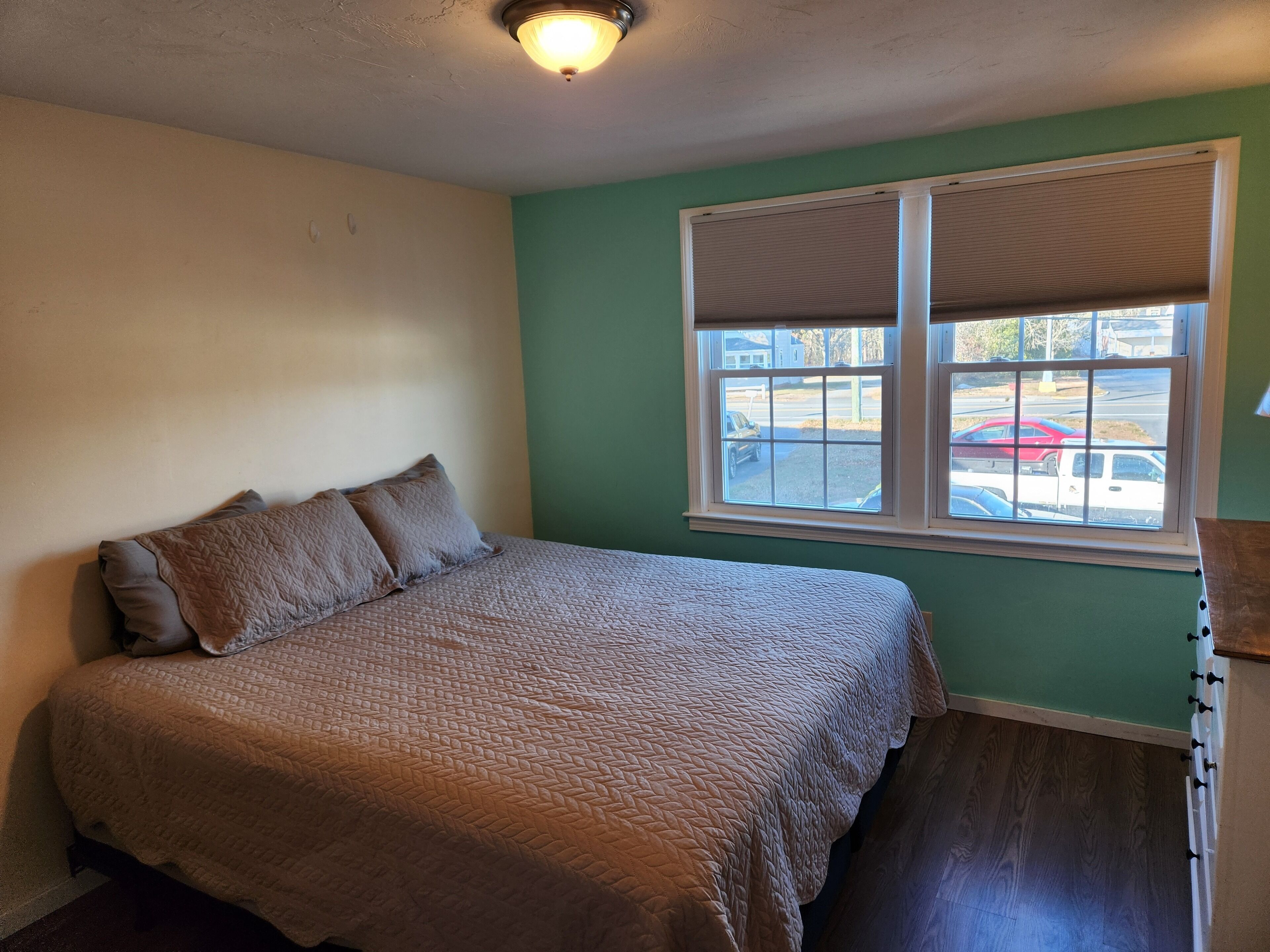 Un dormitorio con una cama, una ventana con persianas y vistas a coches aparcados fuera.