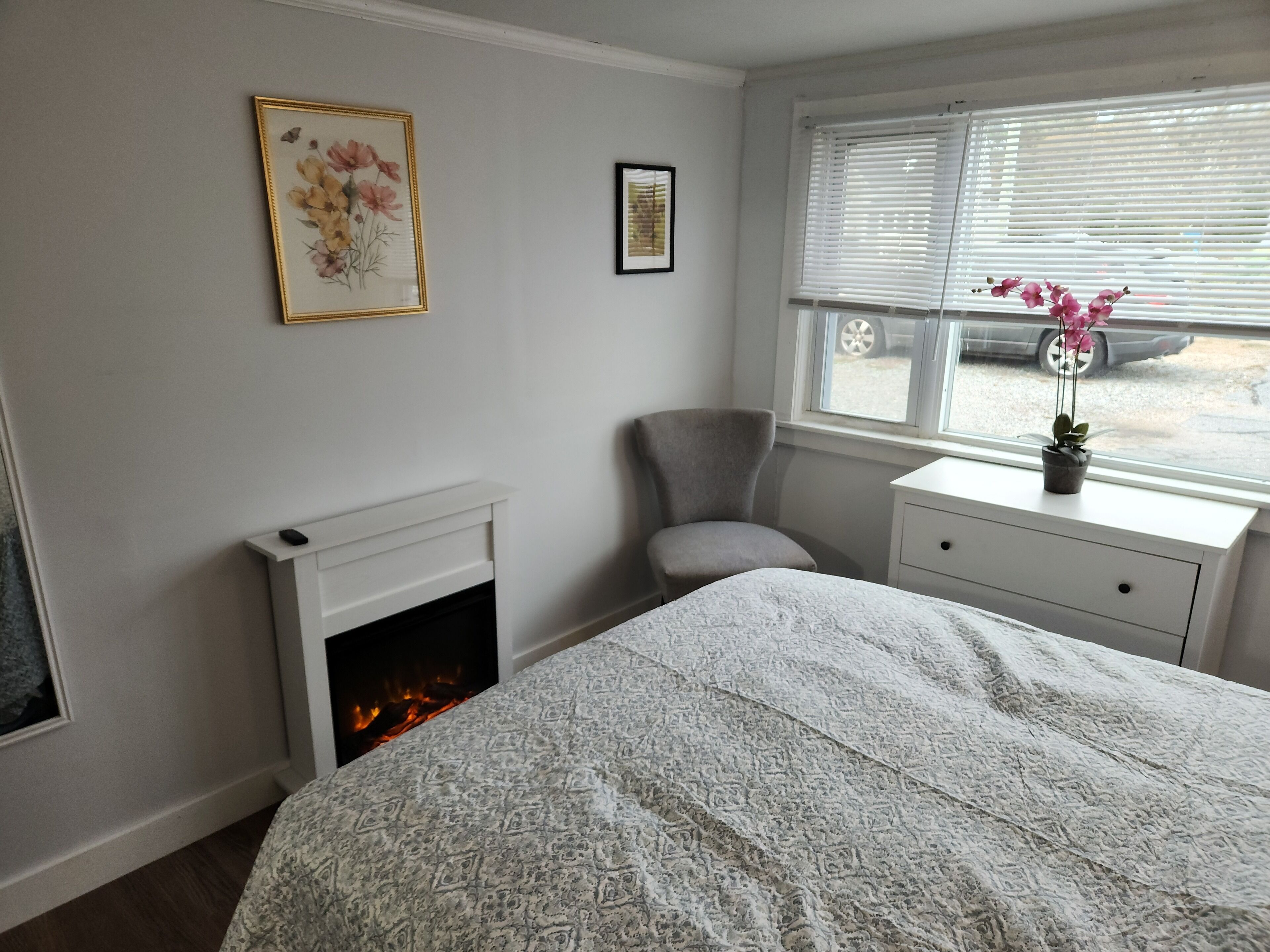 Une chambre à coucher avec une cheminée, un fauteuil, une table de chevet et une fenêtre avec des stores.