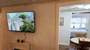 A living room with a fireplace, a television displaying a nature scene, and a dining area with a table and chairs. - Jonathan Edwards Motel (Dennis Port)