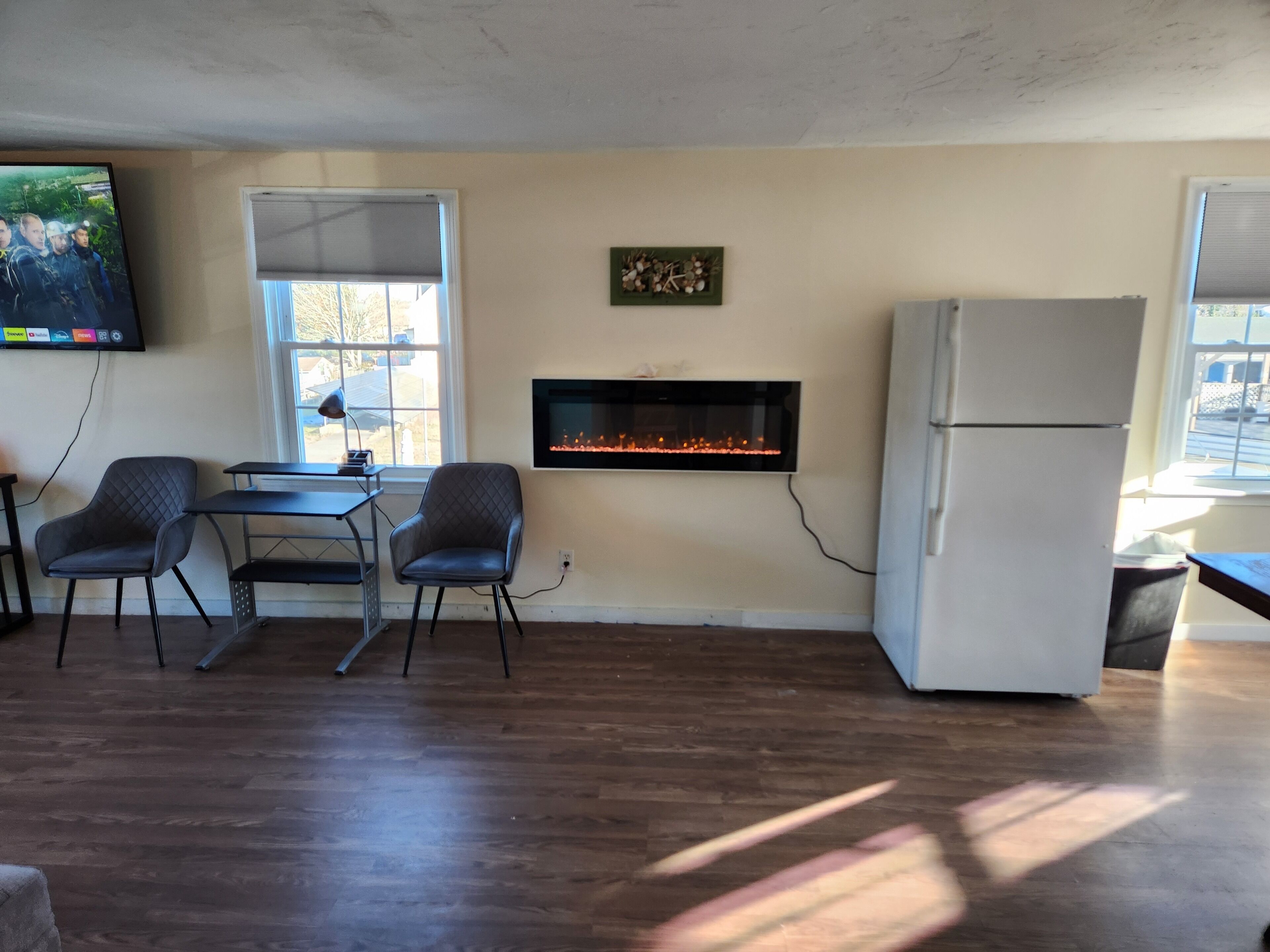 Una habitación con chimenea, televisor montado en la pared, mesa de comedor con sillas y refrigerador.