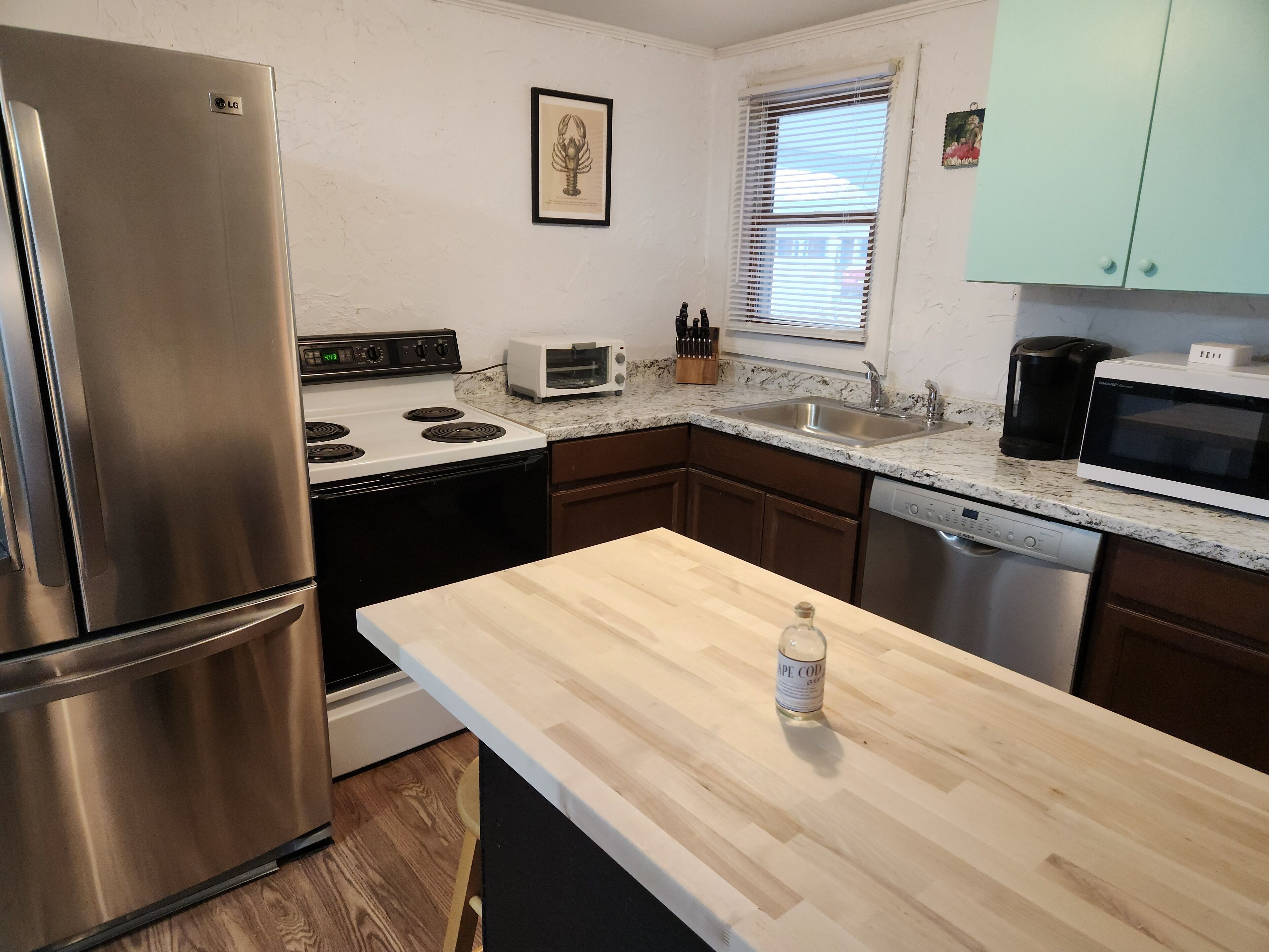 A modern kitchen with stainless steel appliances, a wooden countertop, and a window with blinds.