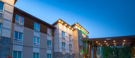 A multi-story hotel with a covered entrance and a parking lot filled with cars.
