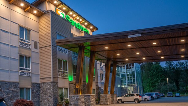 A hotel entrance with a covered parking area, a sign reading "Sandman," and a stone facade. - Sandman Hotel & Suites Squamish (Squamish)