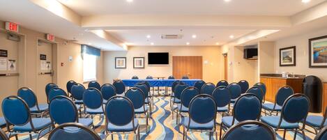 Un salón de conferencias con filas de sillas azules, una mesa larga y una señal de salida.