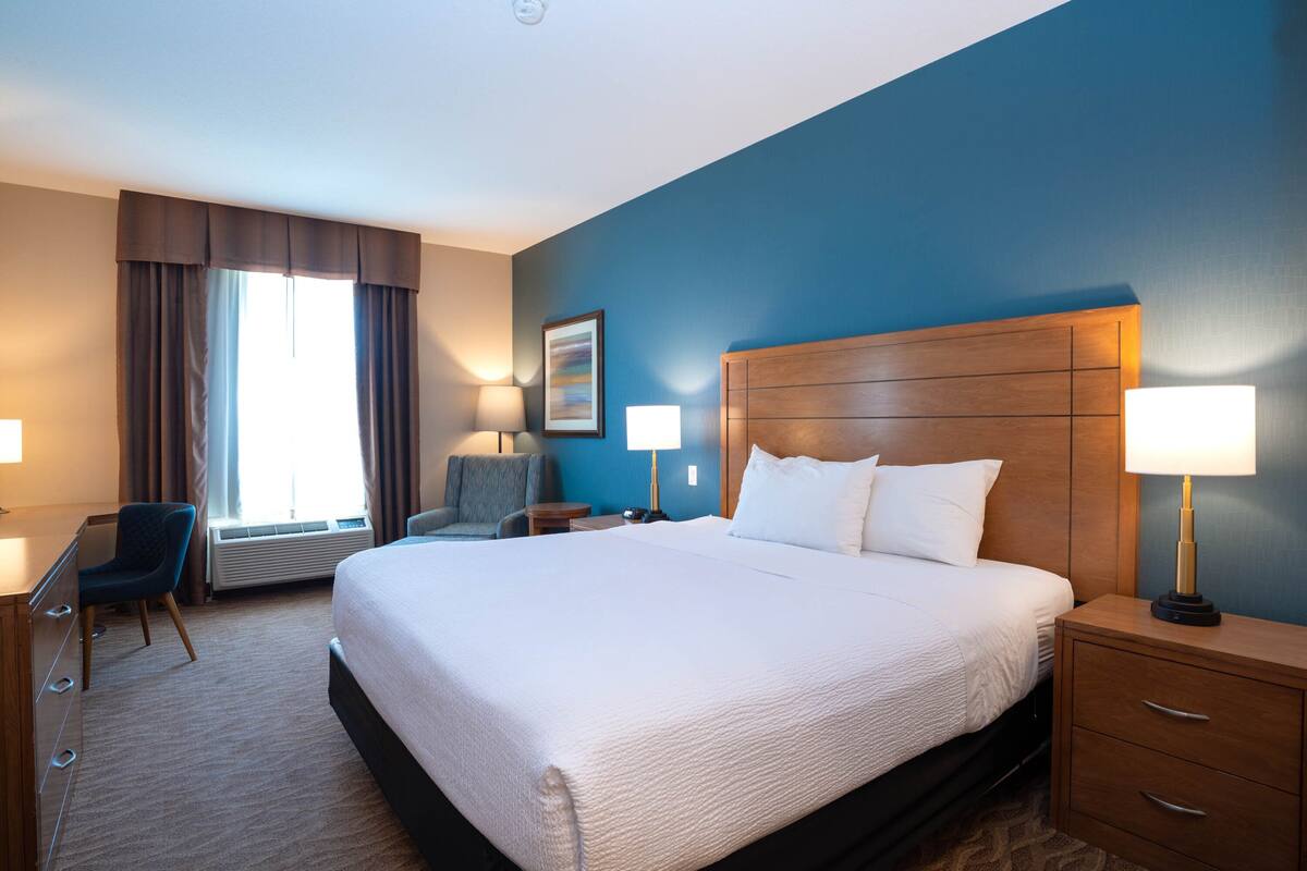 Una habitación de hotel con una cama grande, un escritorio, una silla y una mesita de noche con lámparas.