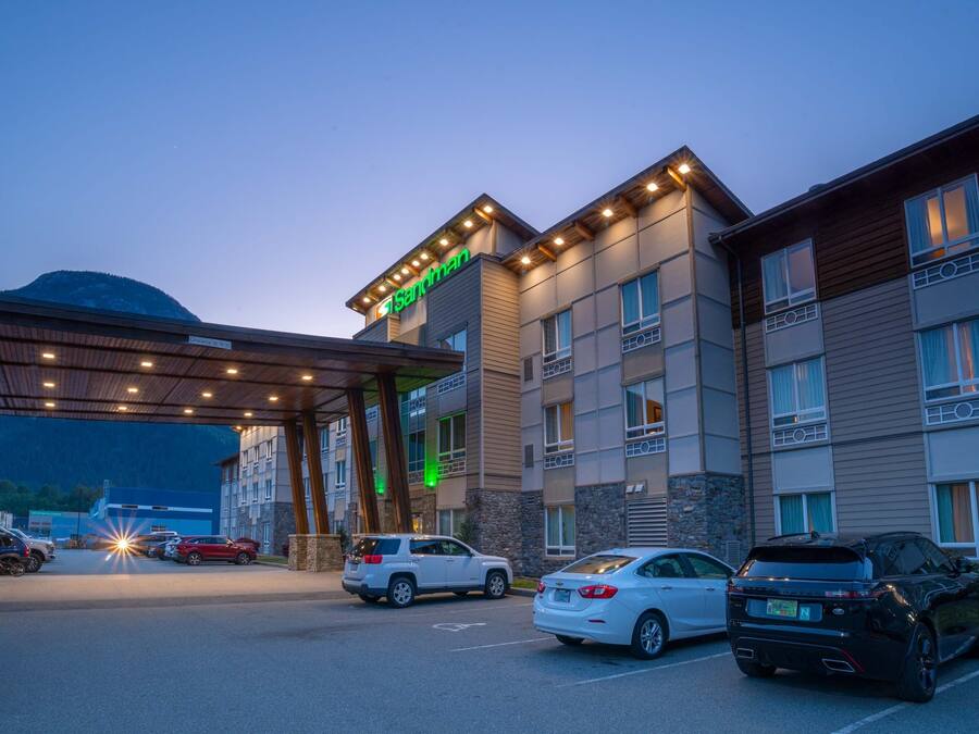 A hotel entrance with a covered driveway, multiple parking spaces, and a mountain in the background.