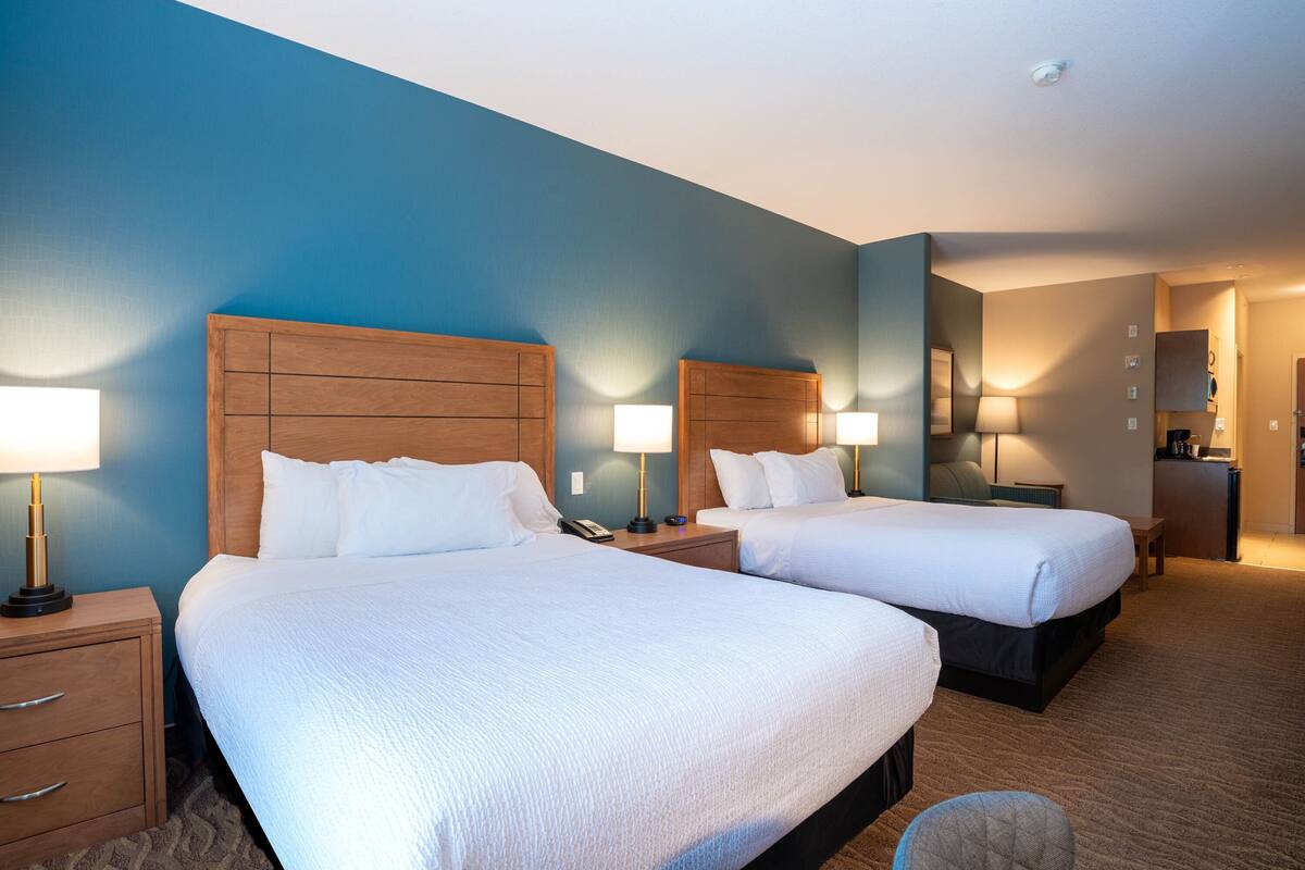 Habitación de hotel con dos camas, cabeceros de madera, lámparas de noche, un escritorio y una pequeña zona de estar.