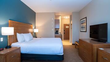 A hotel room with a large bed, wooden nightstands, a television, and a desk with a chair.