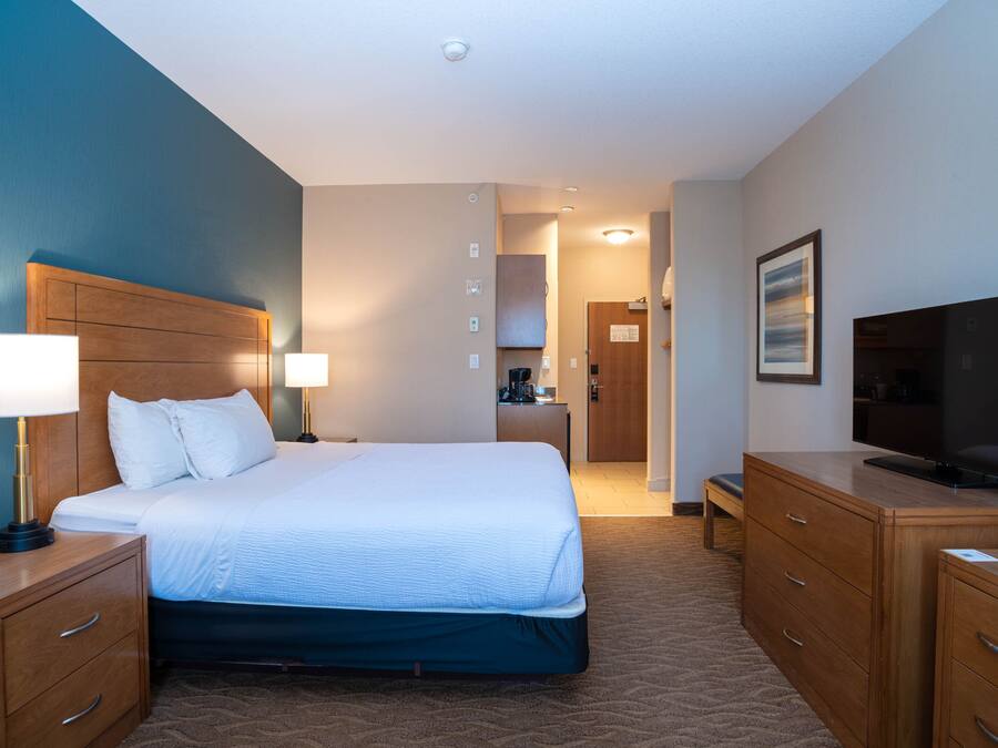 A hotel room with a large bed, wooden nightstands, a television, and a desk with a chair.