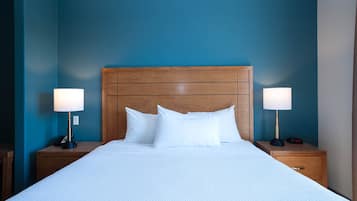 Una cama bien hecha con sábanas blancas, dos lámparas de noche y un cabecero de madera frente a una pared azul.