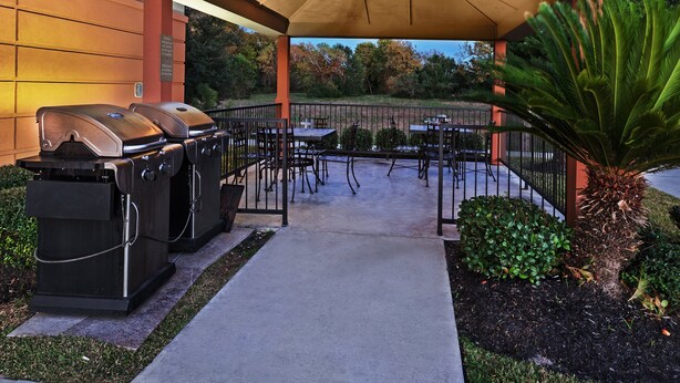 An outdoor patio with a covered seating area, a grill, and a pathway leading to a building.