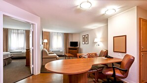 A hotel room with a wooden dining table, chairs, a TV, and a bed.